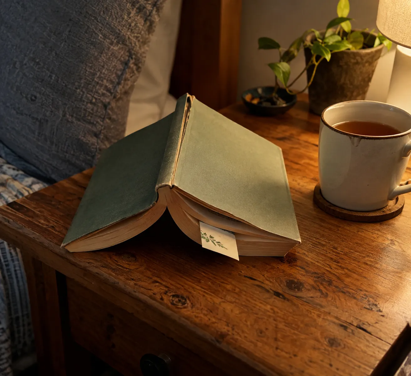 Книга с закладкой на середине и кружка чая на вечернем столике.